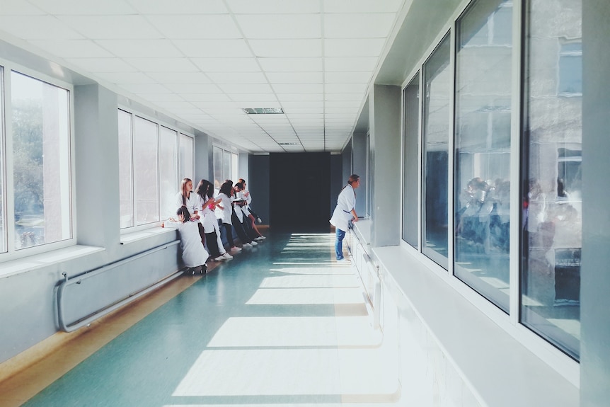 Group of young doctors lean against a wall in a hospital corridor.