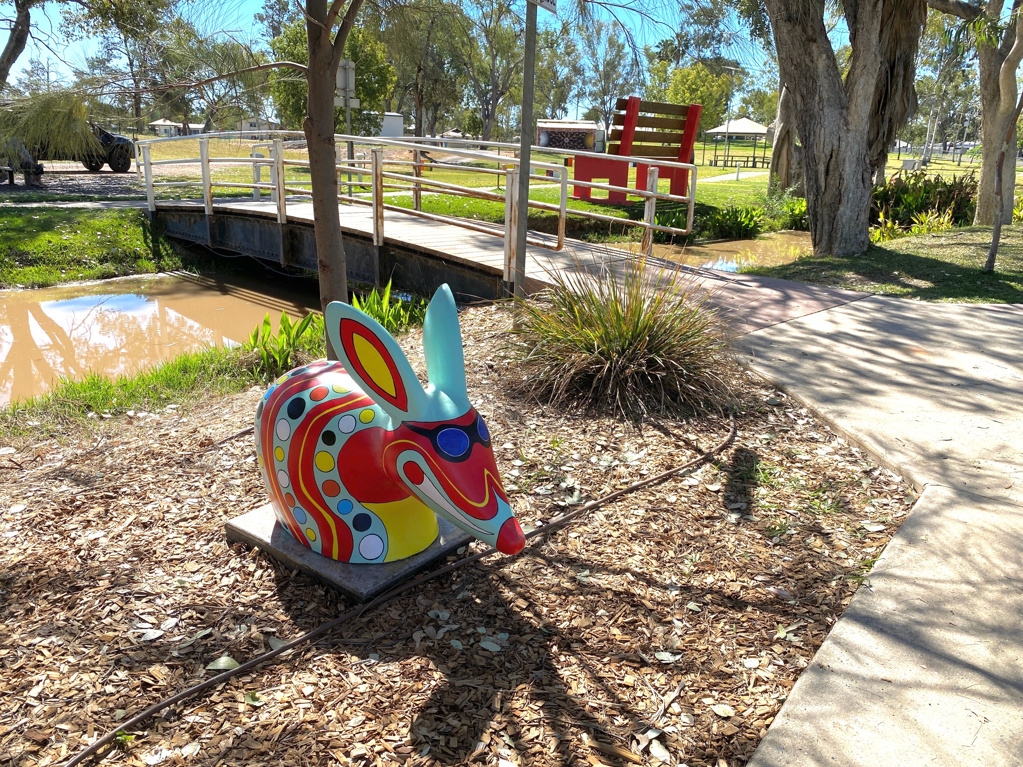 a bilby with painted sunglasses positioned on mulch by a river footbridge