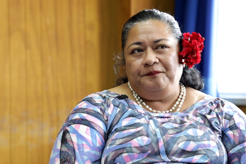 Saui’a Louise Mataia-Milo, a Samoan historian, wears a red flower above her ear and looks off-camera during an interview.