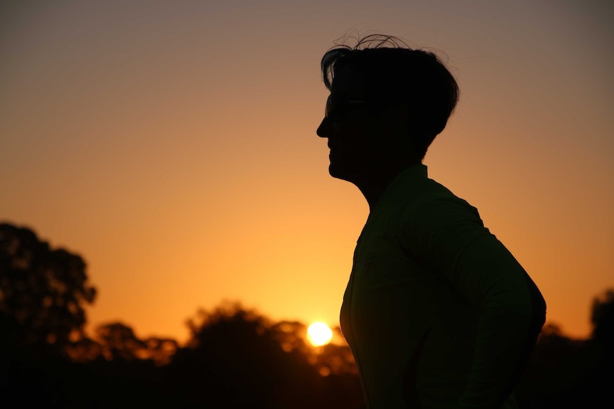 A silhouette of a woman running with the sun setting in the background