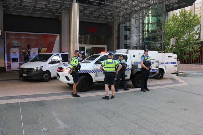 Police stand in front of police vehicles in front of the Westpac bank. Police tape is up.