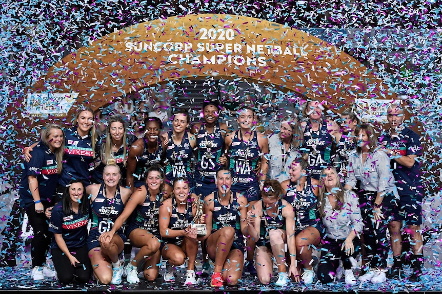 The Super Netball champions celebrate in front of a big banner as confetti falls around them.