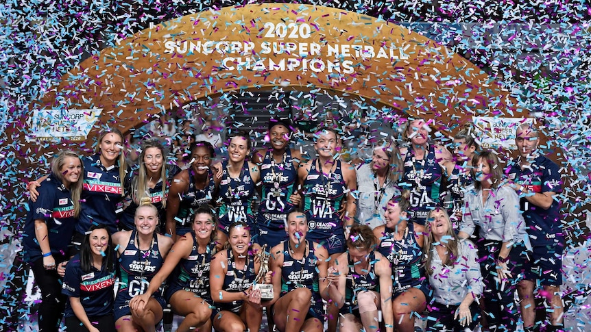 The Super Netball champions celebrate in front of a big banner as confetti falls around them.