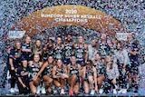 The Super Netball champions celebrate in front of a big banner as confetti falls around them.