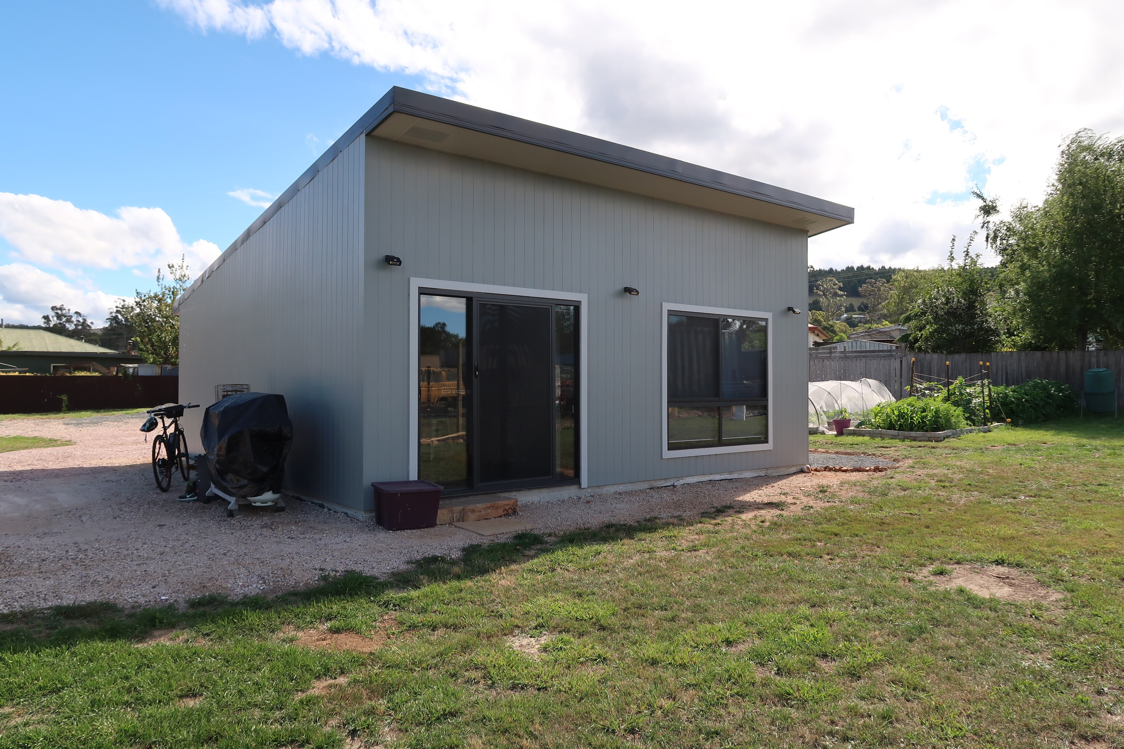 The exterior of a one-bedroom home, adjoining a concrete slab, with a grass lawn in front of it