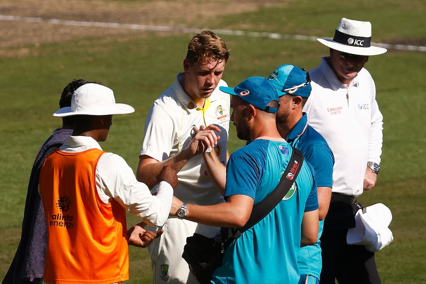 Trainers look at the injured finger of Australia batter Cameron Green during a Test against South Africa.