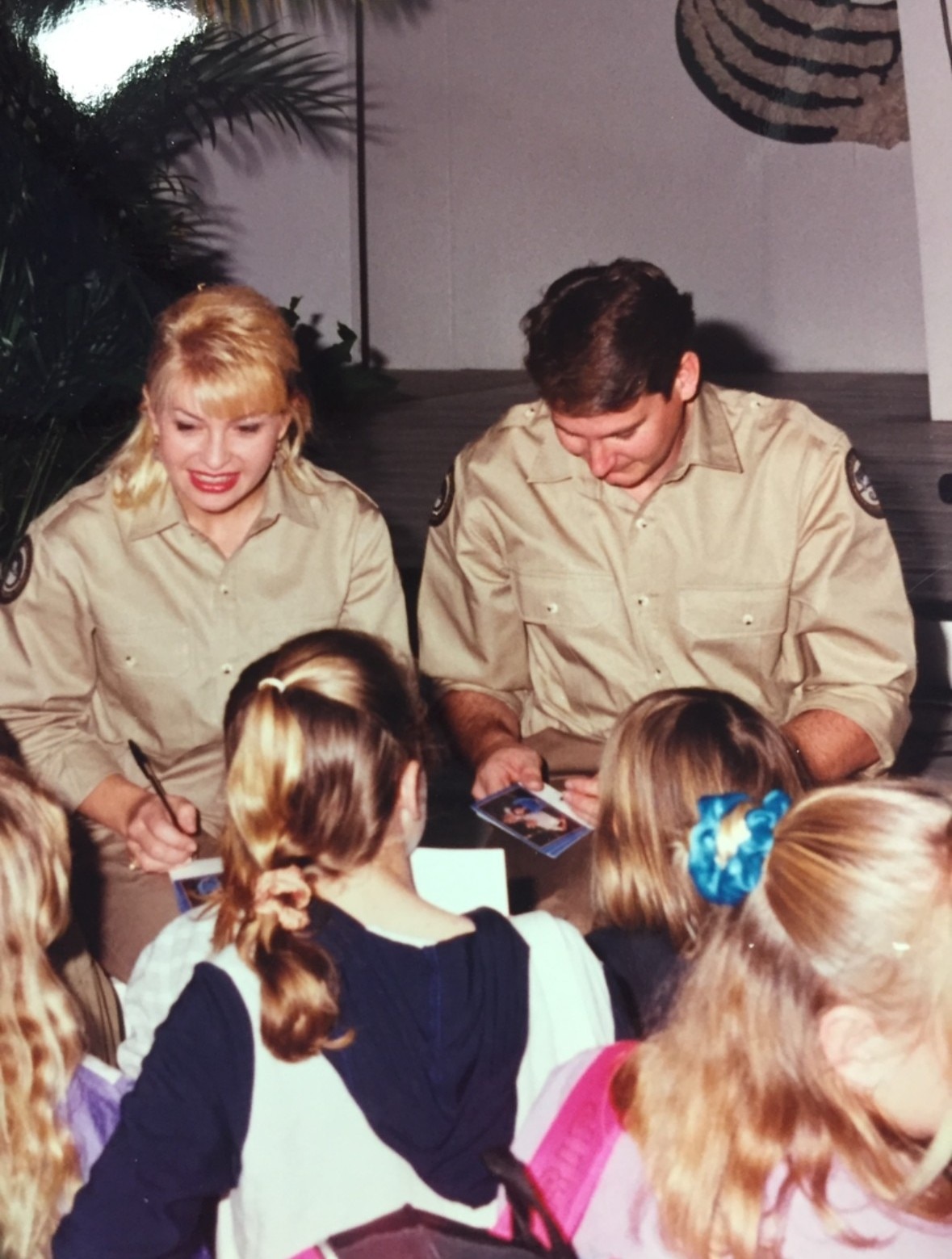 A woman and a man in ranger uniforms signing autographs for a crowd of children.