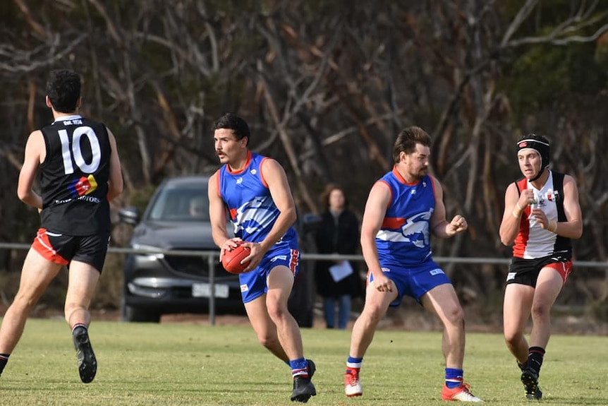 A man wearing a blue and red football jumper holding onto a football. 