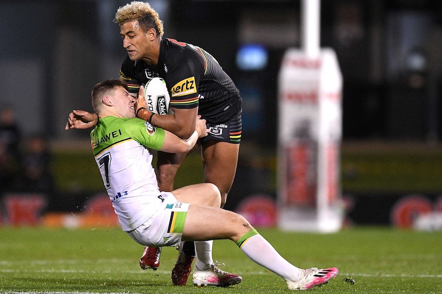 A Penrith Panthers NRL player makes a hit-up as he is tackled by a Canberra Raiders opponent.