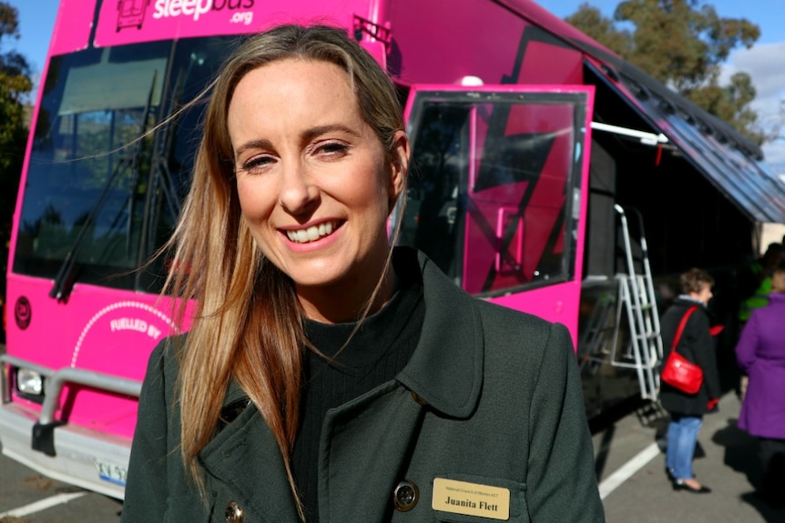 A young woman smiles at the camera in front of the pink Sleepbus.