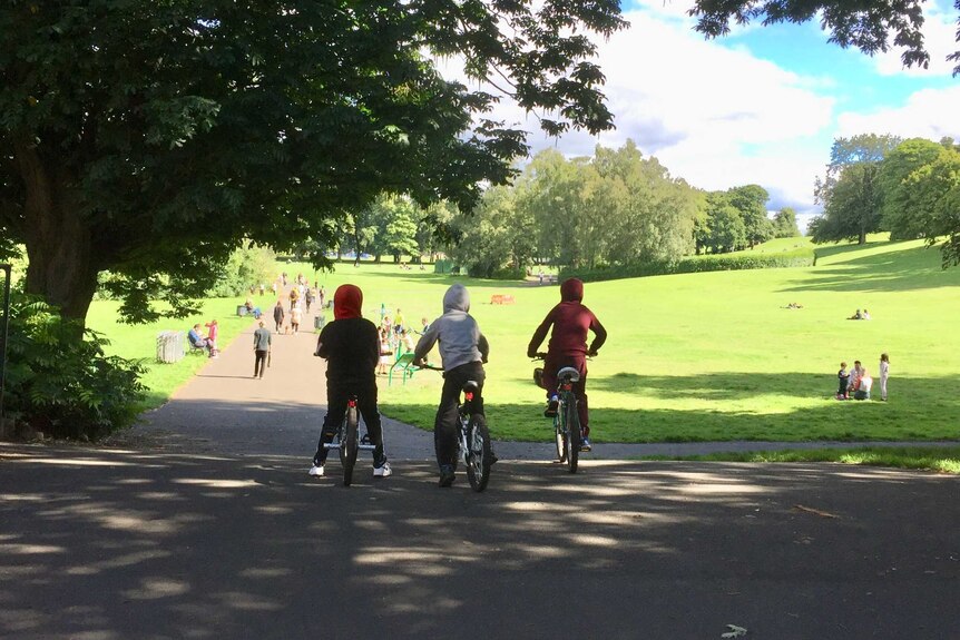 Three boys on their bikes on a path in a Glasgow park in the sunshine