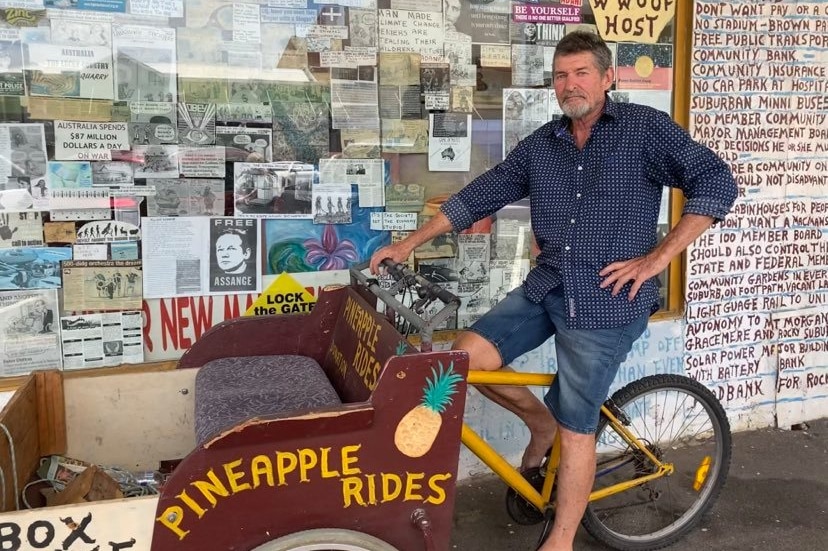 Chris Hooper on a bike in front of shop filled with lots of posters with protest slogans