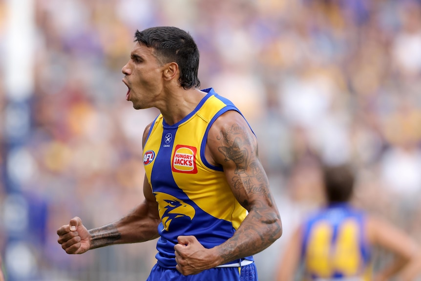 A player in a yellow and blue football jumper celebrates wildly after kicking a goal