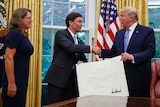 Secretary of Defence Mark Esper shakes hands with Donald Trump as he is sworn in at the Oval Office with his wife beside him.