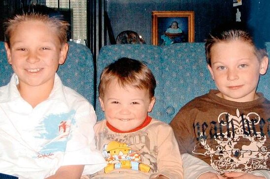 Three smiling young boys sitting on a couch looking at the camera.