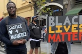 Three people hold protest signs, one reading 'justice 4 injustice' and one saying 'black lives matter'.