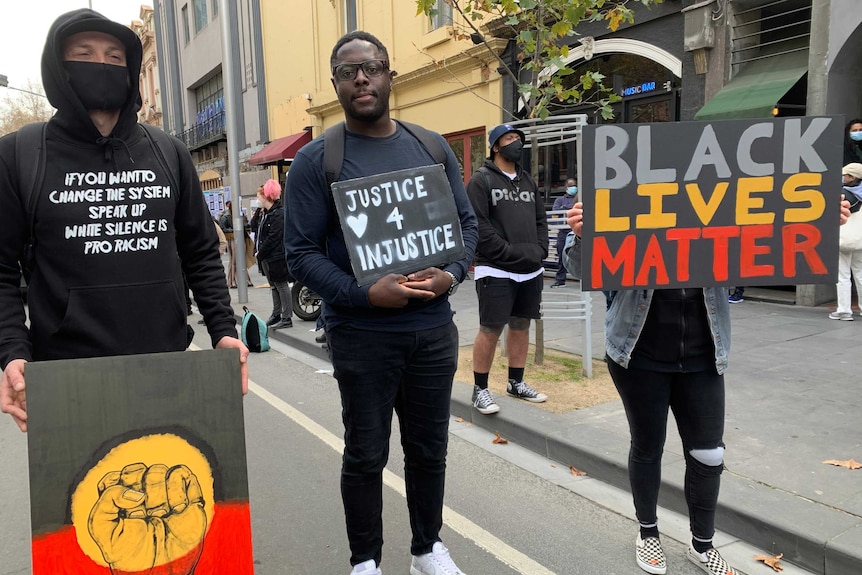 Three people hold protest signs, one reading 'justice 4 injustice' and one saying 'black lives matter'.