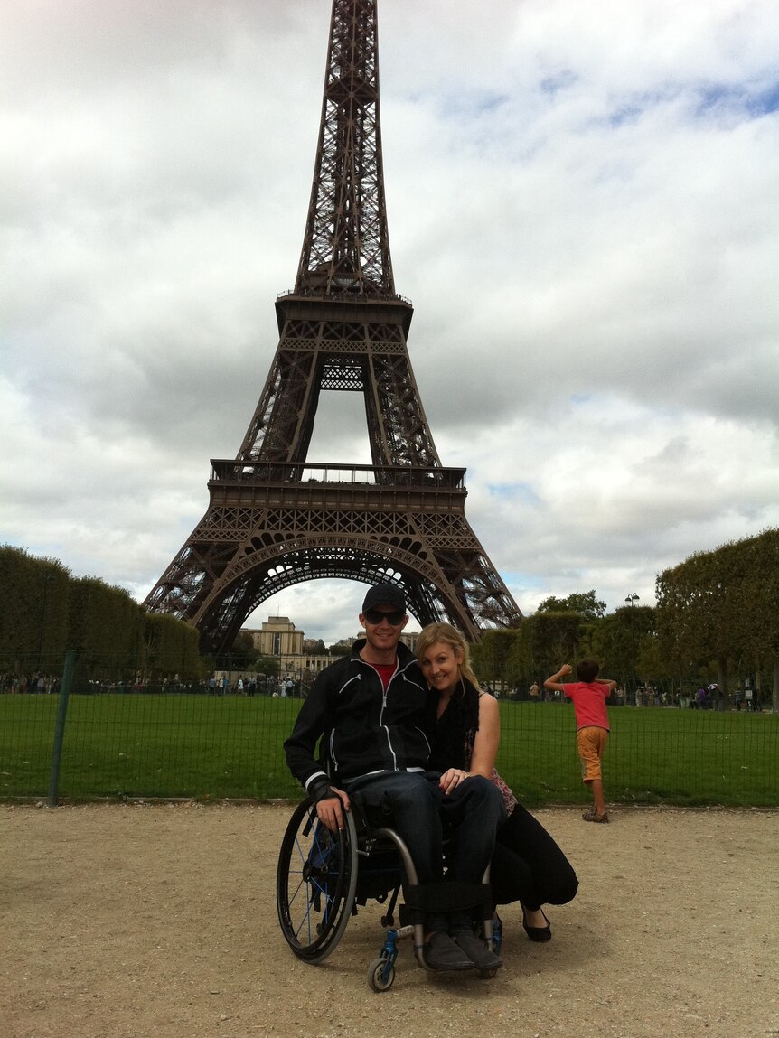 A woman with a man in a wheelchair in front of the Eiffel Tower.