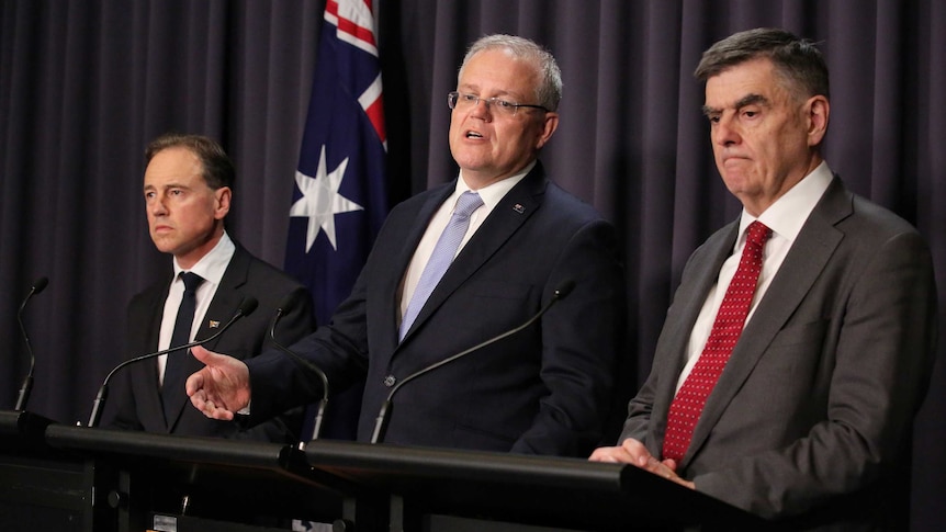Greg Hunt, Scott Morrison and Brendan Murphy stand at podiums in front of a blue curtain