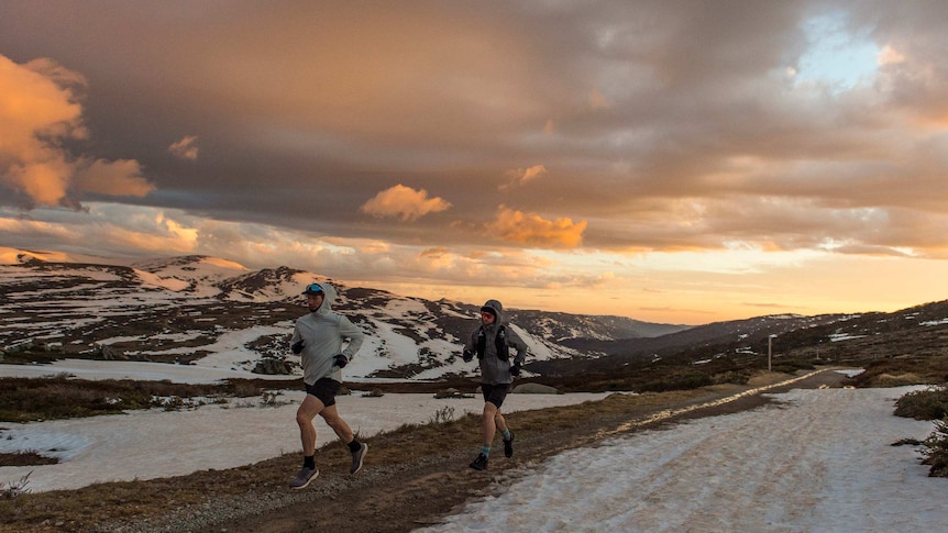 two men running on mountain surrounded by snow and orange sunrise