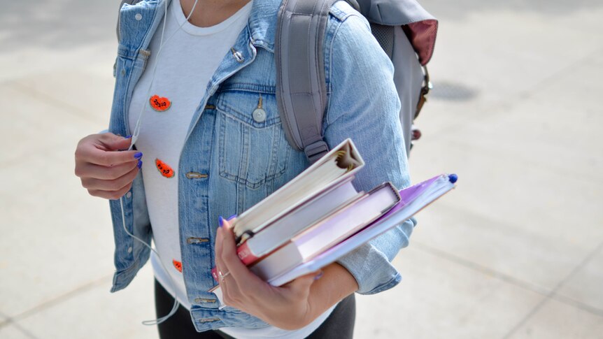 A girl holds textbooks and wears a backpack. 