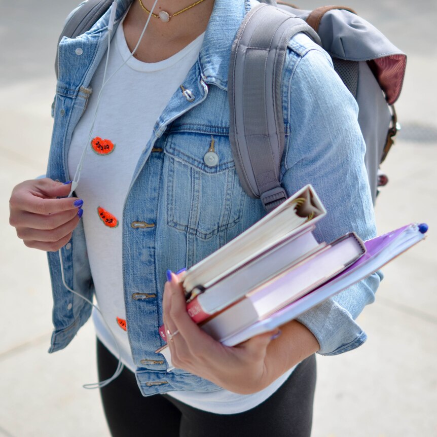 A girl holds textbooks and wears a backpack. 