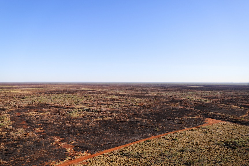 Aerial image shows vivid blue skies and expansive red dirt country scared by bushfire
