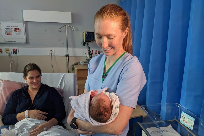 Gold Coast Suns player ALW player Doctor Tiarna Ernst wears scrubs and cradles newborn with mother at hospital.