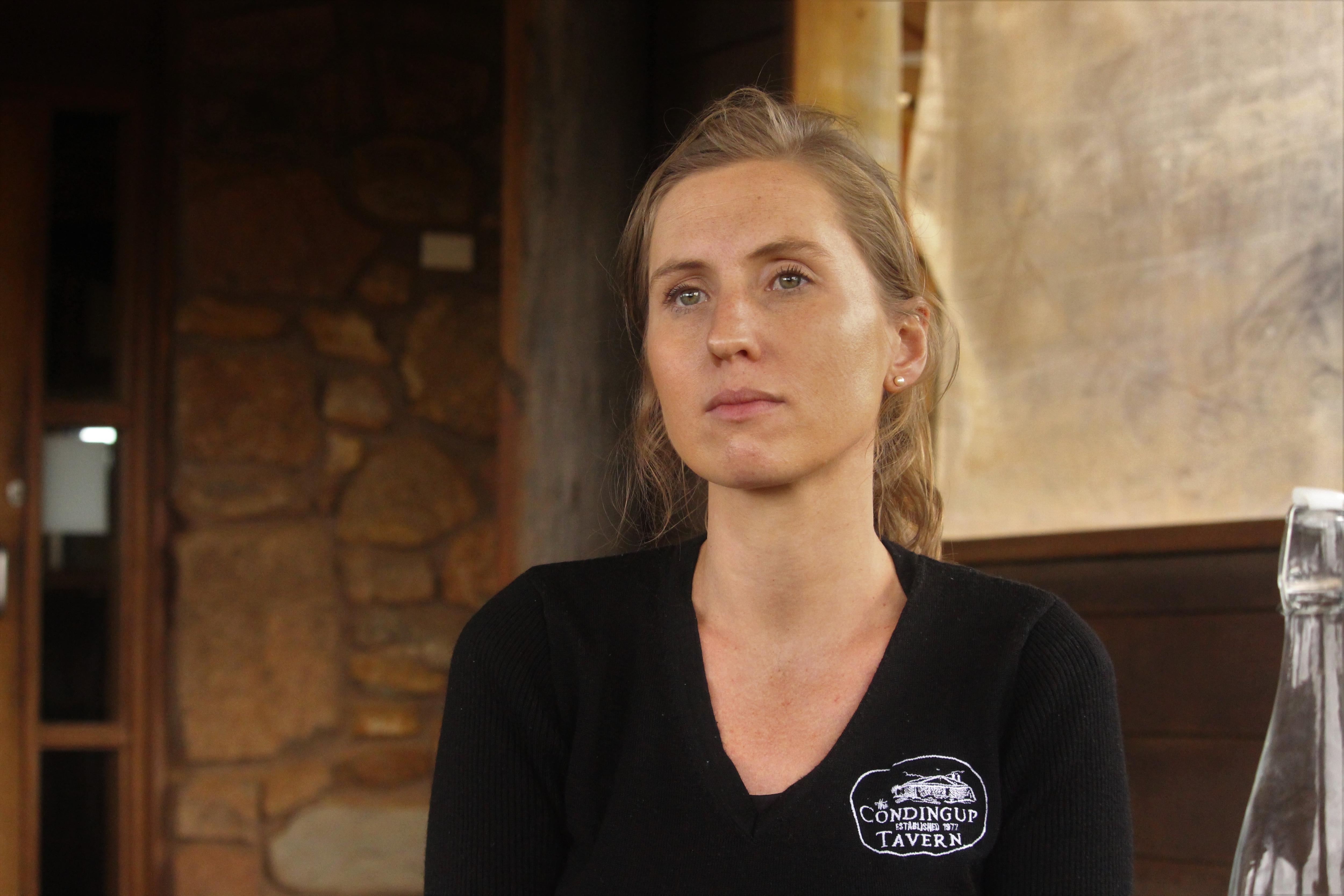 She sits outdoors by a stone wall and stares to the right of the camera