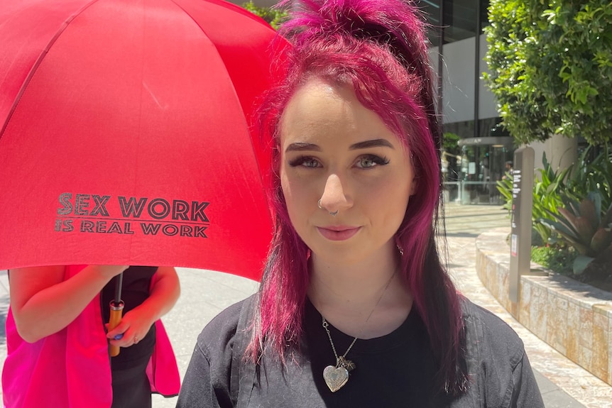 Raven Inferno stands in front of a red umbrella that reads "sex work is real work"