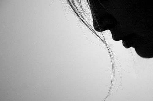 Black and white photo of woman looking down at ground with only some of her face showing.