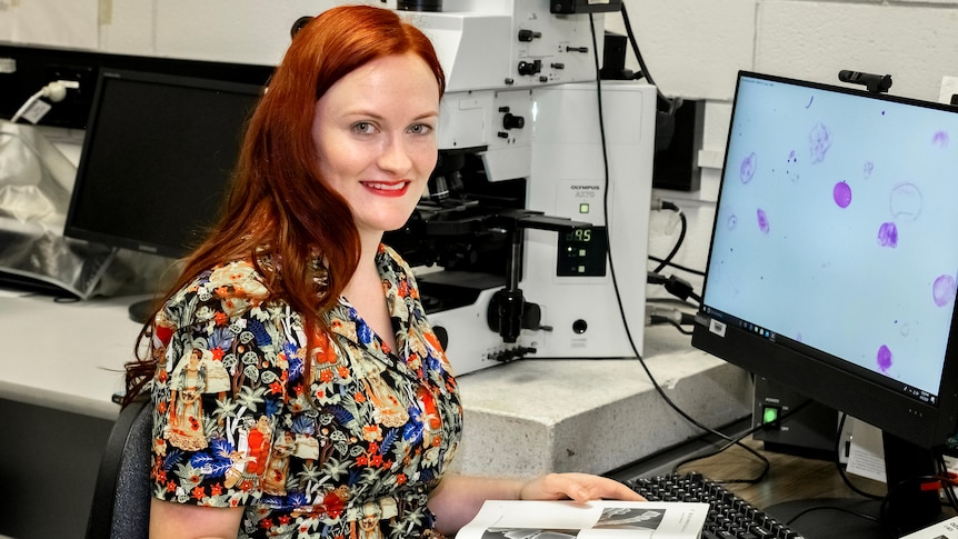 A woman smiling at the camera while sitting in front of a computer.