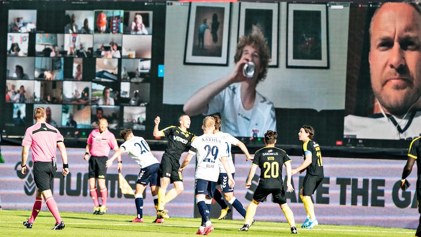 Danish footballers compete for the ball as fans are seen on videoscreens in the background.