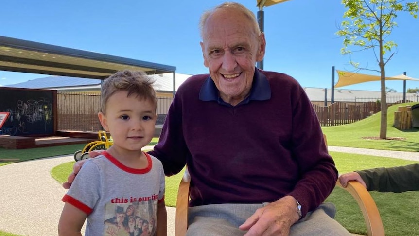 A young boy stands next to an elderly man who is sitting down