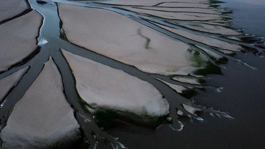 An aerial view shows a tributary stream running through the dried-up flats of a lake