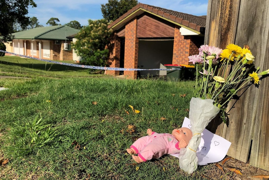 A doll and a bunch of flowers near the front of a house marked off with police tape