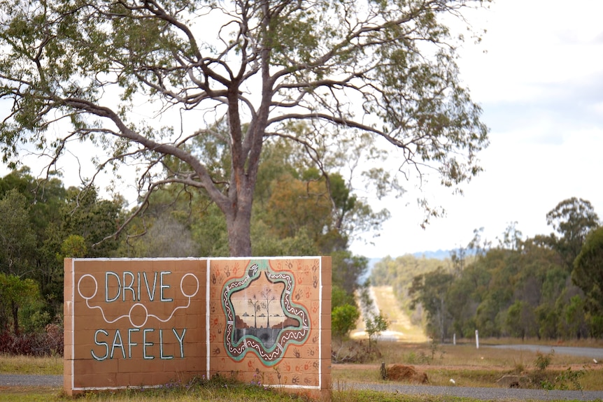 Drive safely sign on the side of the road, trees and a road in the background.