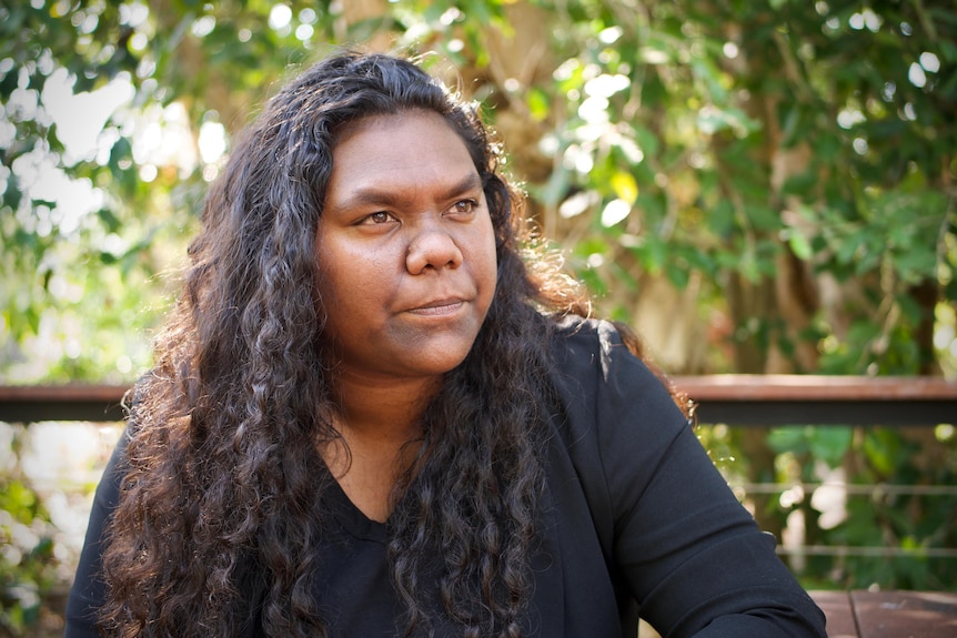 A young Aboriginal woman with long curly hair looks into the distance