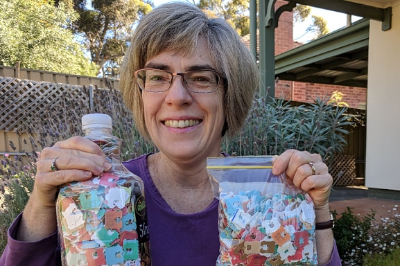 Jenny Cooper smiles while holding up two bags filled with bread tags