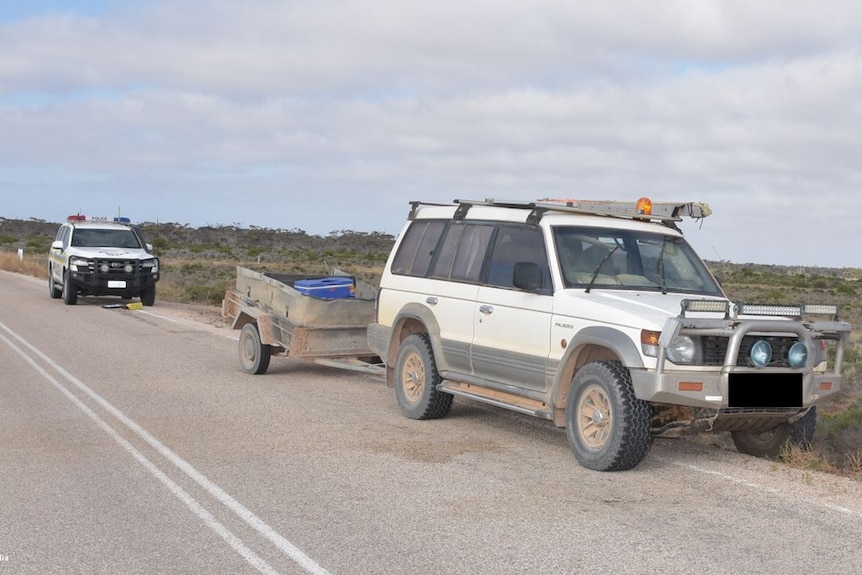 a white 4wd abandoned on the road side with a police vehicle behind it