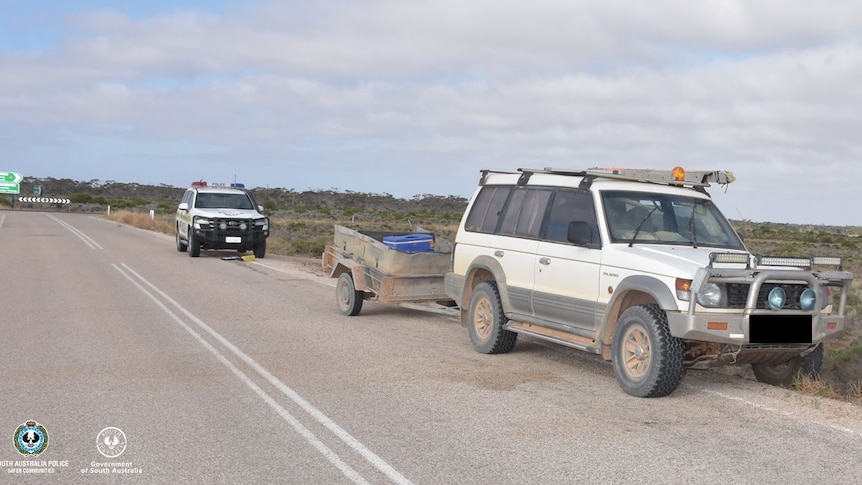 a white 4wd abandoned on the road side with a police vehicle behind it