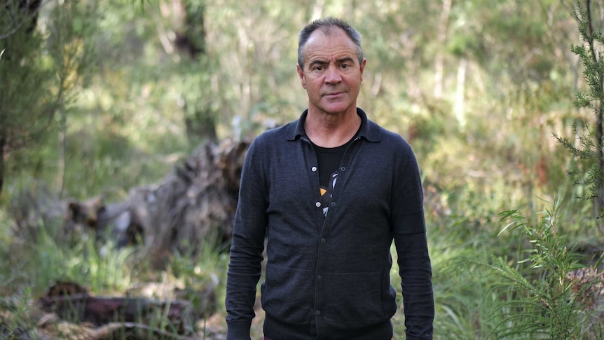 The writer Kim Scott standing in front of the Australian bush, looking concerned