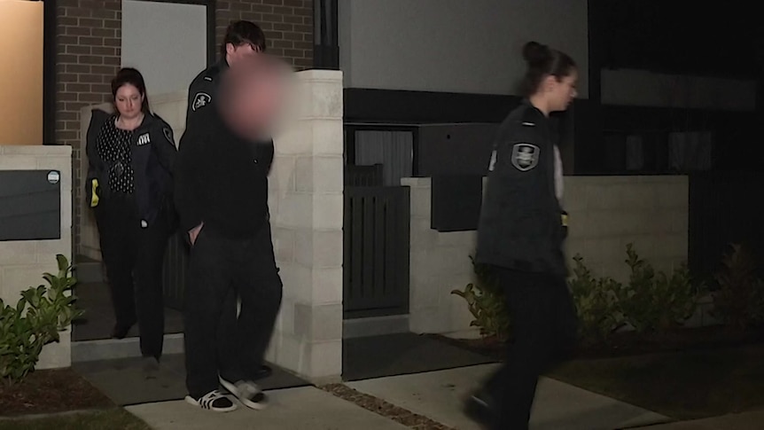 A blurred man in handcuffs with detectives.