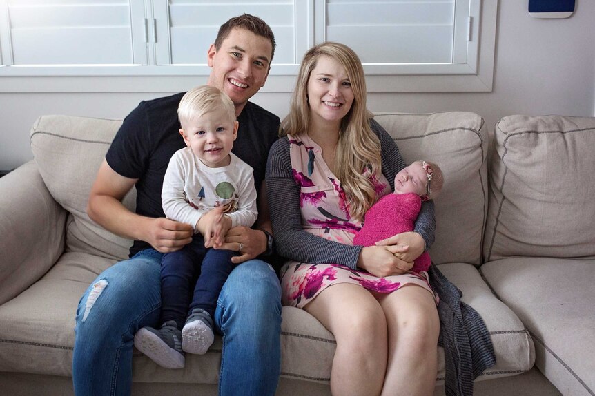 Local mum Amy Steenbergen and her husband and two children sit on their lounge.