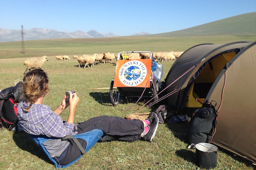 Angela Maxwell sits alone by her campsite overlooking a field of cattle