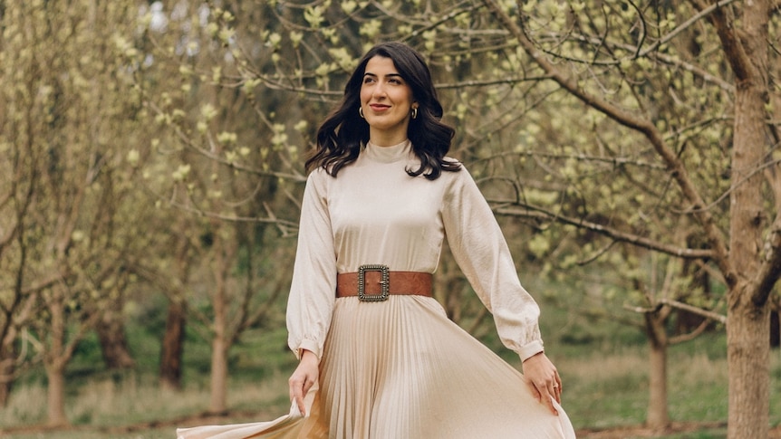 Vocalist Olivia Chamoun in a cream dress, surrounded by green trees