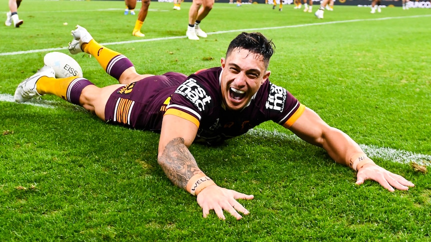 A Brisbane Broncos NRL player slides along the ground after scoring a try.