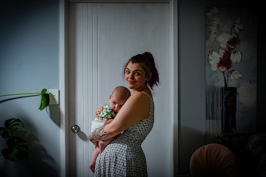 Jess cradles a baby in her arms, smiling warmly at the camera.