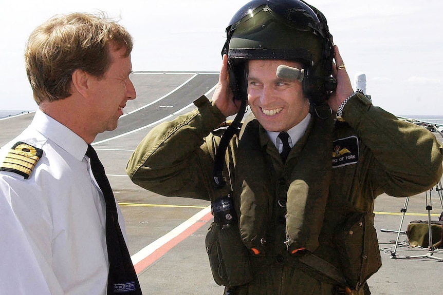 Prince Andrew removes a helmet as he talks to a man aboard HMS Ark Royal.
