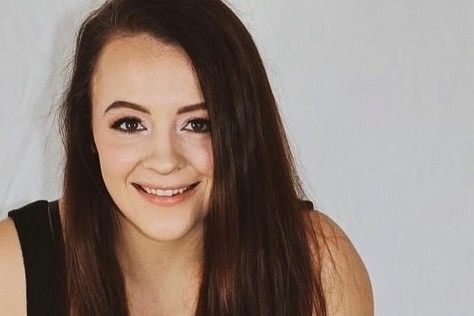 woman wearing a black tank top, has brunette hair and is smiling at the camera. 